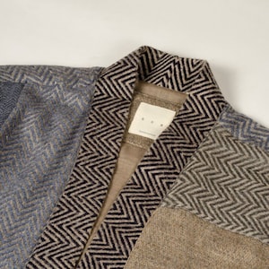 Peut inclure: Un cardigan marron, bleu et noir à motif chevron. Le cardigan a un col et une étiquette qui indique "K.O.B. handcrafted".