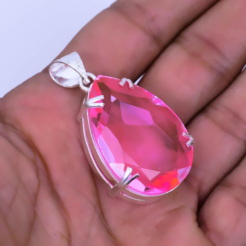 May include: A teardrop-shaped pendant with a pink gemstone set in a silver frame.