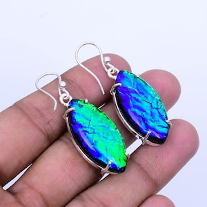 May include: A pair of silver dangle earrings with iridescent blue and green glass oval drops. The glass has a crackled texture.