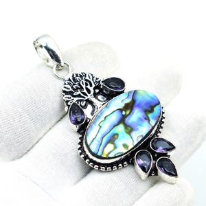 May include: A silver pendant featuring an oval abalone shell with iridescent blues and greens. Accented with purple amethyst stones and a tree of life design. The pendant is approximately 2 inches long.