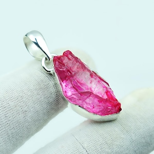 Op de afbeelding: Zilveren hanger met een ruwe, roze edelsteen. De hanger heeft een gepolijste zilveren zetting en balein. Het ruw gesneden kristal toont een heldere roze tint en wordt gepresenteerd op een witte achtergrond.