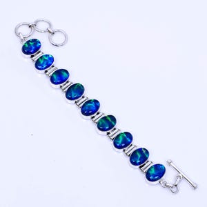 May include: A silver bracelet with a toggle clasp features oval-shaped blue and green opal gemstones.