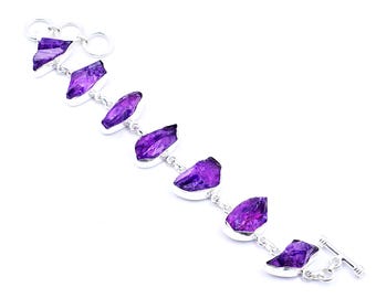 May include: A silver bracelet with striking purple gemstones. The gemstones are an irregular shape and set in silver bezels, connected by silver links. The bracelet has a toggle clasp. The gemstones have a natural, raw appearance.