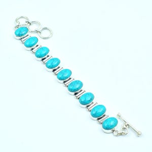 Peut inclure: Un bracelet en argent orné de pierres ovales turquoise. Le bracelet est doté d'un fermoir à bascule et d'une série de pierres ovales turquoise serties dans de l'argent. Le bracelet est conçu avec une série de pierres ovales turquoise reliées par des maillons en argent.