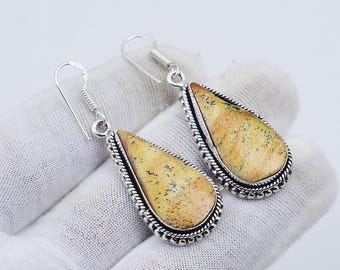 May include: A pair of teardrop-shaped earrings. Each earring features a light yellow stone with dark speckles, set in a silver-colored metal frame with a rope-like border. The earrings are displayed on a white surface.