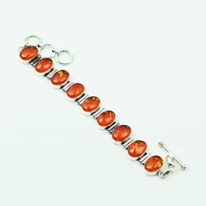 Op de afbeelding: Een zilveren armband met ovale barnstenen. De barnstenen hebben een warme oranje-bruine kleur en zijn gezet in een zilveren metalen zetting. De armband heeft een tuimelsluiting.
