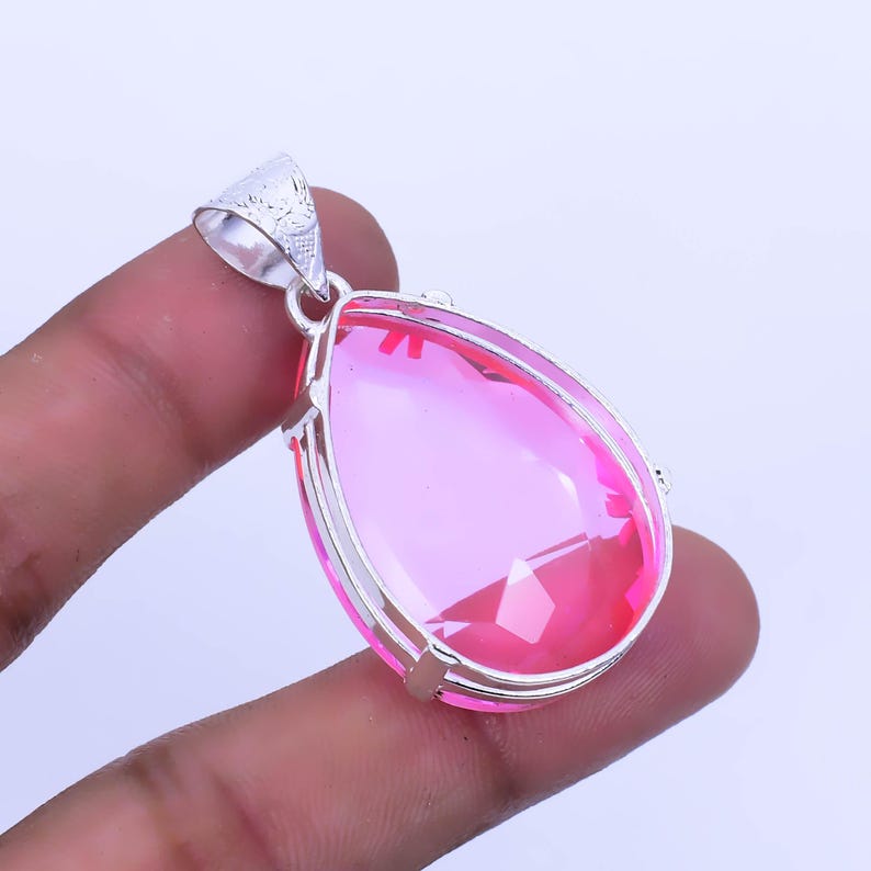 May include: A teardrop-shaped pendant with a pink crystal set in a silver frame.