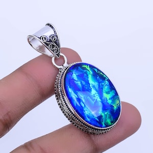 May include: A silver pendant with an oval-shaped blue opal gemstone. The pendant has an intricate silver design around the gemstone.