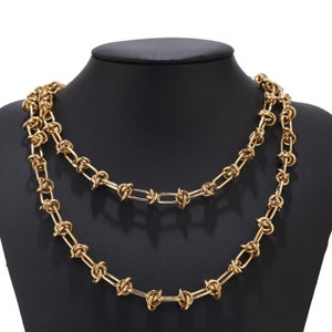May include: A gold-toned chain necklace with a knotted design. The necklace is layered and has a chunky, bold look.