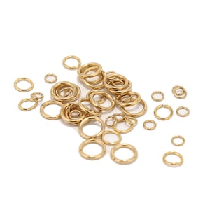 May include: A large assortment of gold jump rings of various sizes. The jump rings are scattered on a white surface.