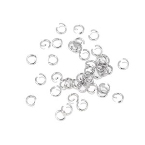 May include: A scattering of silver jump rings, a type of jewellery finding used for connecting chains, cords, and other jewellery components.