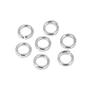 May include: Seven silver jump rings, also known as split rings, are arranged on a white surface. These rings are commonly used in jewelry making and crafting.