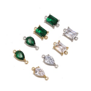 May include: Assortment of clear and green crystal connector charms with gold and silver accents. The charms feature a variety of shapes, including square, rectangle, and teardrop.