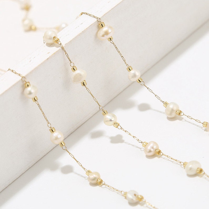 Puede incluir: Un delicado collar de cadena dorada con perlas blancas. La cadena est&aacute; hecha de peque&ntilde;os c&iacute;rculos unidos y las perlas est&aacute;n espaciadas uniformemente.