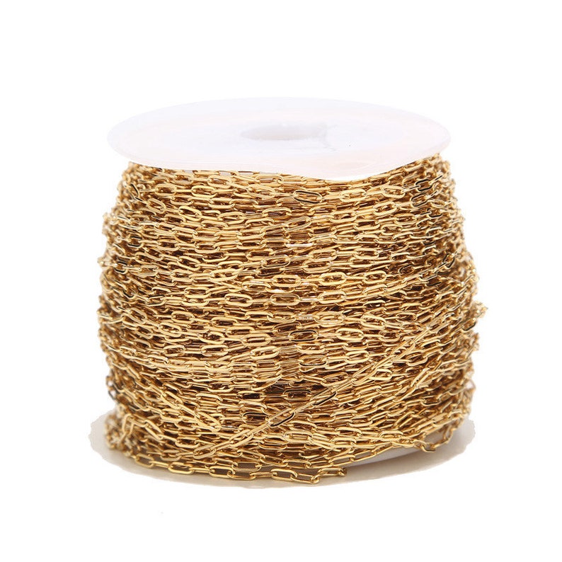 Op de afbeelding: Een spoel van goudkleurige ketting met ovale schakels. De ketting is strak gewikkeld rond een witte plastic spoel. De ketting heeft een heldere, glanzende goudkleur en de schakels zijn uniform van grootte en vorm. Deze ketting is geschikt voor het maken van sieraden.