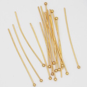 May include: A group of gold head pins with round heads. The pins are arranged in a random pattern on a white background.