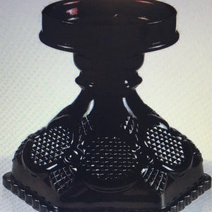 May include: Black glass candle holder with a geometric design. The holder has a round top and a triangular base.