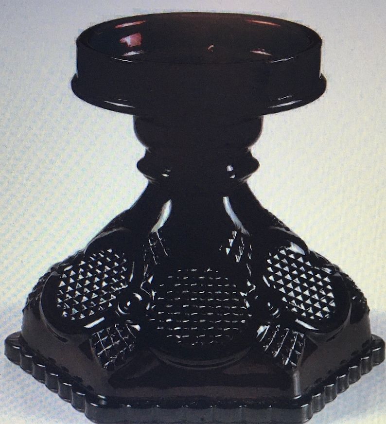 May include: Black glass candle holder with a geometric design. The holder has a round top and a triangular base.