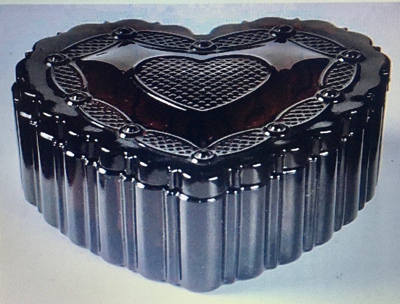 May include: A black heart-shaped glass trinket box with a raised, patterned heart design on the lid. The box has a ribbed texture around the sides.