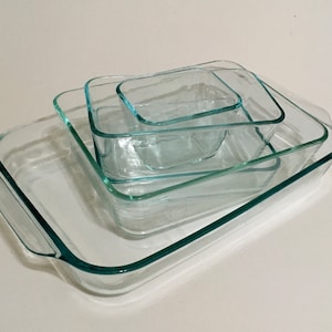 May include: Four clear glass baking dishes of different sizes stacked on top of each other. The dishes are rectangular and have a smooth, clear finish.