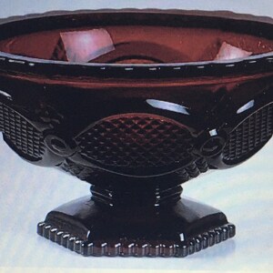 May include: A dark red glass bowl with a pedestal base. The bowl has a diamond pattern and a scalloped edge.