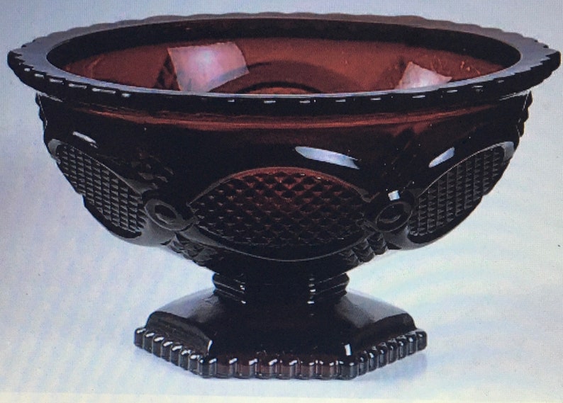 May include: A dark red glass bowl with a pedestal base. The bowl has a diamond pattern and a scalloped edge.