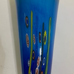 May include: A blue glass vase with a textured surface and colourful abstract designs. The vase has a wide mouth and a narrow base.