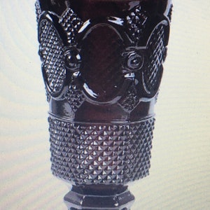 May include: A dark purple glass vase with a diamond pattern and intricate designs. The vase has a wide mouth and a square base.