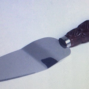 May include: A silver cake server with a brown, intricately carved wooden handle.