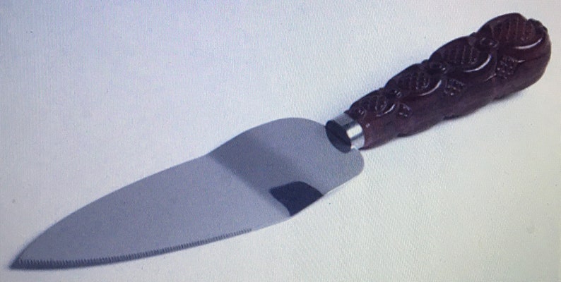 May include: A silver cake server with a brown, intricately carved wooden handle.