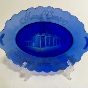 May include: A blue glass plate with a white etched image of Mount Vernon, the home of George and Martha Washington. The plate has a scalloped edge.