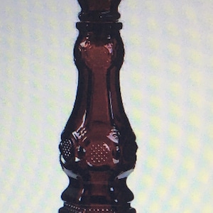 May include: A dark red glass candle holder with a decorative design. The holder has a wide base and a tall, slender stem.
