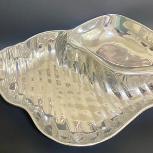 Puede incluir: Un plato de servir de plata con forma de concha marina con un cuenco grande y poco profundo en el centro.