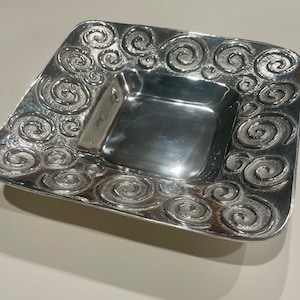 Può includere: Un piatto da portata quadrato in argento con un motivo decorativo a spirale attorno al bordo.