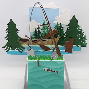 May include: A papercraft scene with a fishing theme. The design includes a fishing rod, a boat with oars, trees, clouds, and a fish. The colour palette features shades of green, blue, and brown, creating a serene outdoor setting.