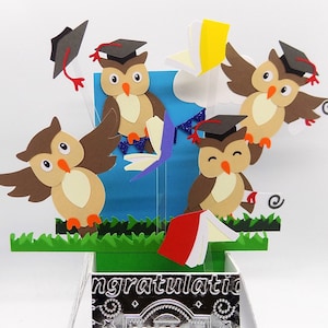 Può includere: Un biglietto pop-up a tema laurea con quattro gufi marroni che indossano cappelli da laurea e tengono libri e diplomi. Il biglietto ha uno sfondo blu con coriandoli viola e argentati e la parola "Congratulazioni" sul davanti.