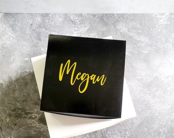 May include: A black gift box with a white label. The label has the name "Megan" written in gold lettering.