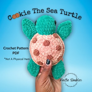 May include: Crochet pattern PDF for a plush sea turtle named "Cookie the Sea Turtle". The turtle is green with a pink shell with brown spots. The pattern is not a physical item.