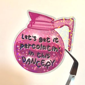 May include: A pink, glittery sticker in the shape of a coffee pot. The sticker has the text "Let's get it percolatin' in this DANCERY" in a playful font. The sticker is being held by tweezers.
