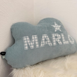 Könnte beinhalten: Ein wolkenförmiges Kissen aus weichem, hellblauem Cordstoff. Der Name "MARLO" ist in weißen Vichy-Buchstaben auf dem Kissen geschrieben. Ein weißer Vichy-Stern ist ebenfalls auf dem Kissen.