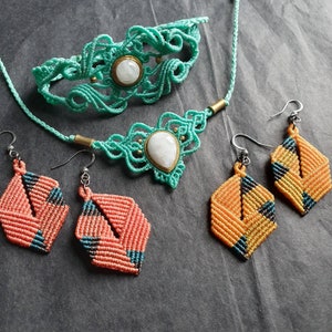 Peut inclure: Un ensemble de trois bijoux en macramé, comprenant un collier, un bracelet et des boucles d'oreilles. Le collier et le bracelet sont bleu turquoise et ornés d'une pierre de lune blanche. Les boucles d'oreilles sont orange et jaunes avec des accents noirs.