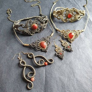 Könnte beinhalten: Ein Set aus drei Halsketten und Ohrringen mit roten Edelstein-Akzenten. Die Halsketten sind aus braunem Kordel gefertigt und weisen komplizierte Knotenmuster auf. Die Ohrringe sind ebenfalls aus braunem Kordel gefertigt und haben ein baumelndes Design.