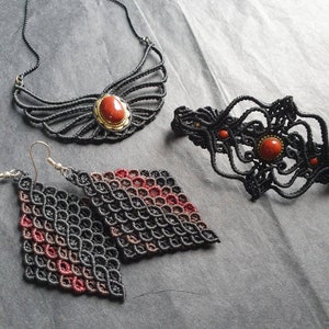 May include: A set of three jewelry pieces featuring black macrame with red gemstone accents. The set includes a necklace, a bracelet, and a pair of earrings.