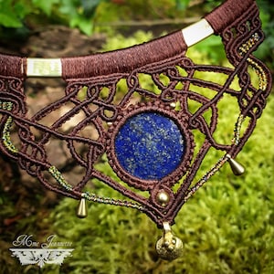 May include: A brown macrame necklace with a large blue lapis lazuli stone pendant and gold accents. The necklace is decorated with small gold beads and has a gold clasp.