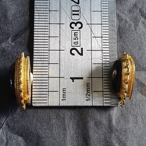 May include: Two gold-toned cufflinks with red and black gemstones. The cufflinks are measured against a ruler, showing they are approximately 1/2 inch in diameter.