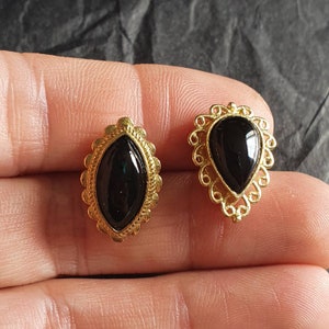 May include: A pair of gold-tone earrings with black oval-shaped stones set in ornate filigree designs.
