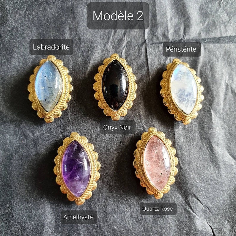 May include: Six different gemstone cabochons set in gold-toned bezels. The stones are labradorite, onyx, moonstone, amethyst, rose quartz, and peristerite.  The stones are all oval shaped and have a smooth, polished finish.  The bezels are ornate and have a detailed design.  The stones are arranged in a row on a dark gray background.  The text "Mod&egrave;le 2" is at the top of the image.
