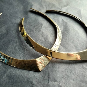 May include: Two gold-toned metal collars, one with a hammered finish and the other with a smooth, polished finish. Both collars are open in the back and have a pointed, V-shaped front.
