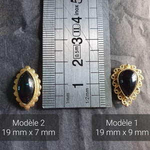 May include: Two gold-toned metal embellishments with black glass stones. The embellishment on the left is oval-shaped and measures 19 mm by 7 mm. The embellishment on the right is teardrop-shaped and measures 19 mm by 9 mm.