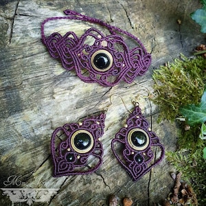 May include: A set of purple macrame jewelry with black gemstone accents. The set includes a choker necklace and a pair of earrings.